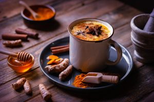 cup of golden milk with turmeric root and cinnamon stick