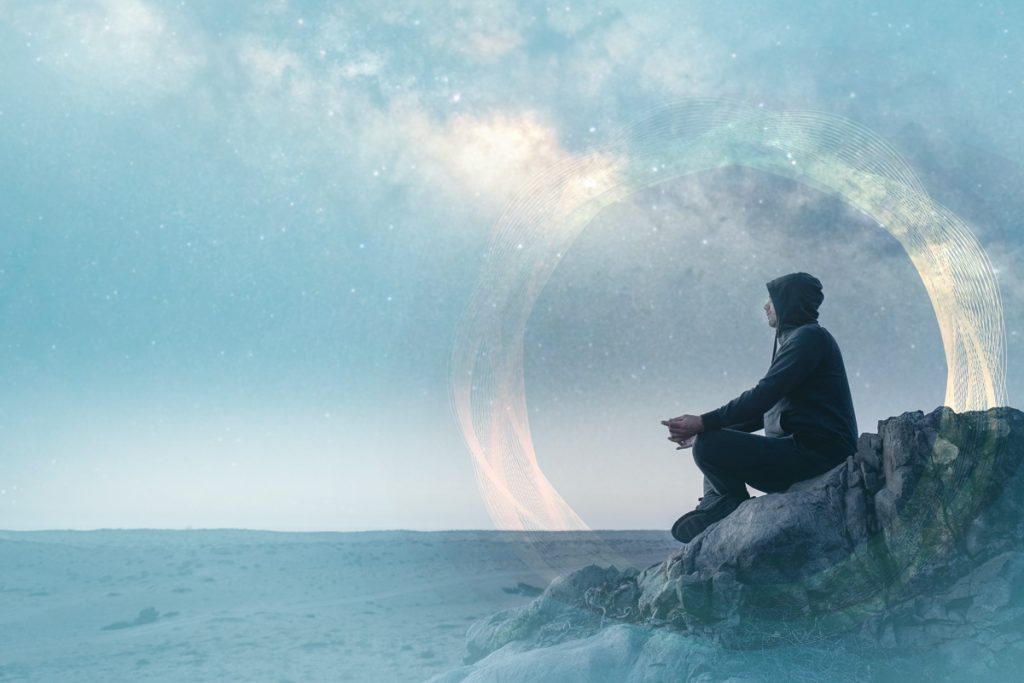 man sitting on a cliff contemplating life with the night sky above and behind him