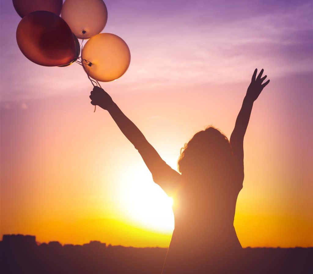 woman with her arms up holding air balloons in the sunset