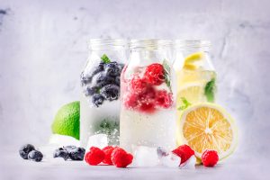 3 glass bottles with fruit and water, ice around it and slices of fruit