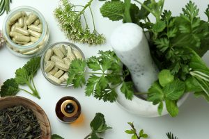mortar, pestle, herbs and supplement pills on a white table