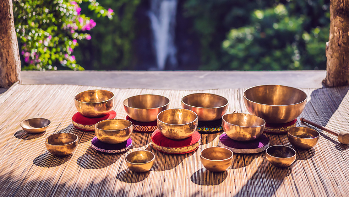 13 sound bowls on a mat in front of a waterfall and a bougainvilla bush on the left