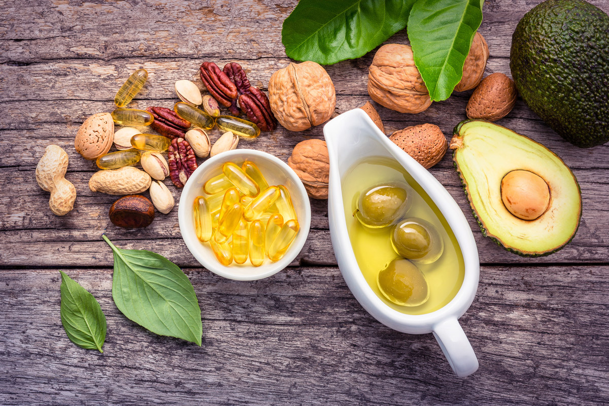 dietary fats on a wooden surface: olive oil, avocados, nuts